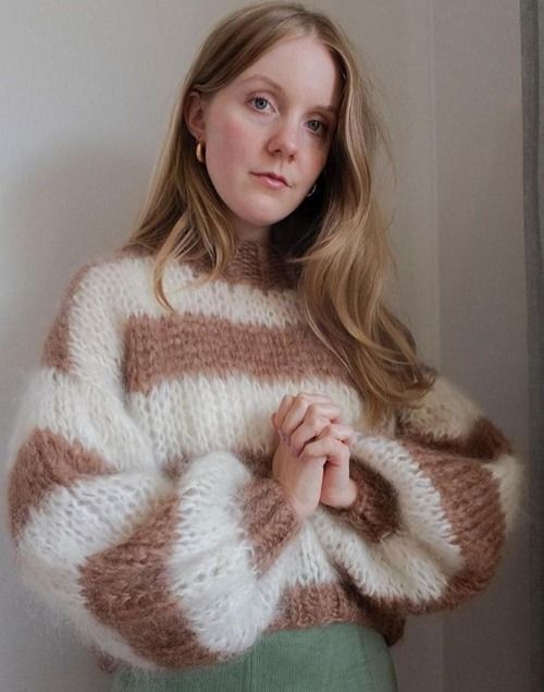 a woman standing in front of a window wearing a sweater