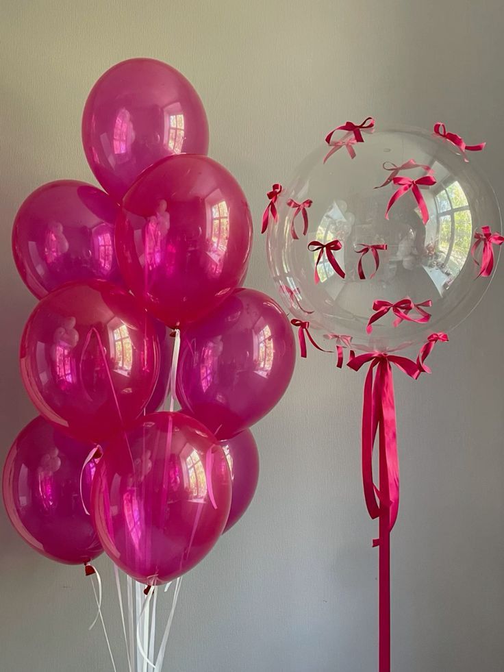 a bunch of balloons that are in front of a balloon stand with pink ribbons on it