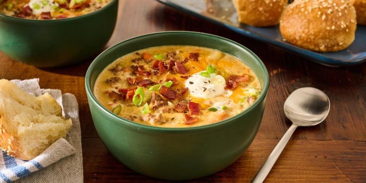 two green bowls filled with soup next to bread on a wooden table and spoons