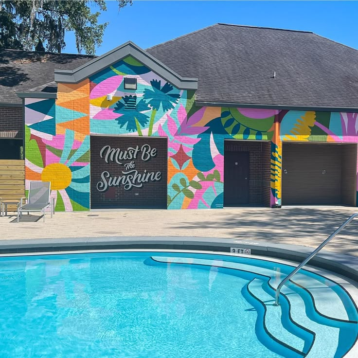 an empty swimming pool in front of a multicolored building that says must be sunshine