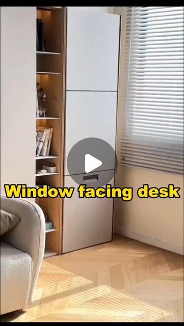 a living room with a couch, book shelf and window facing desk in the corner