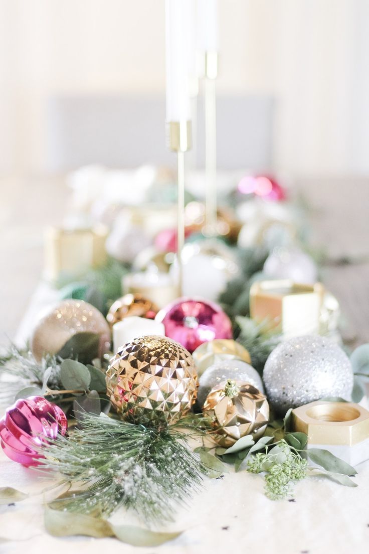 a white table topped with lots of christmas ornaments and greenery next to a candle