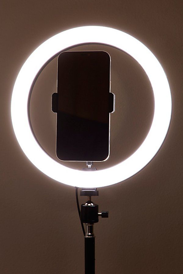 a circular light with a cell phone attached to it's side and a tripod in the foreground