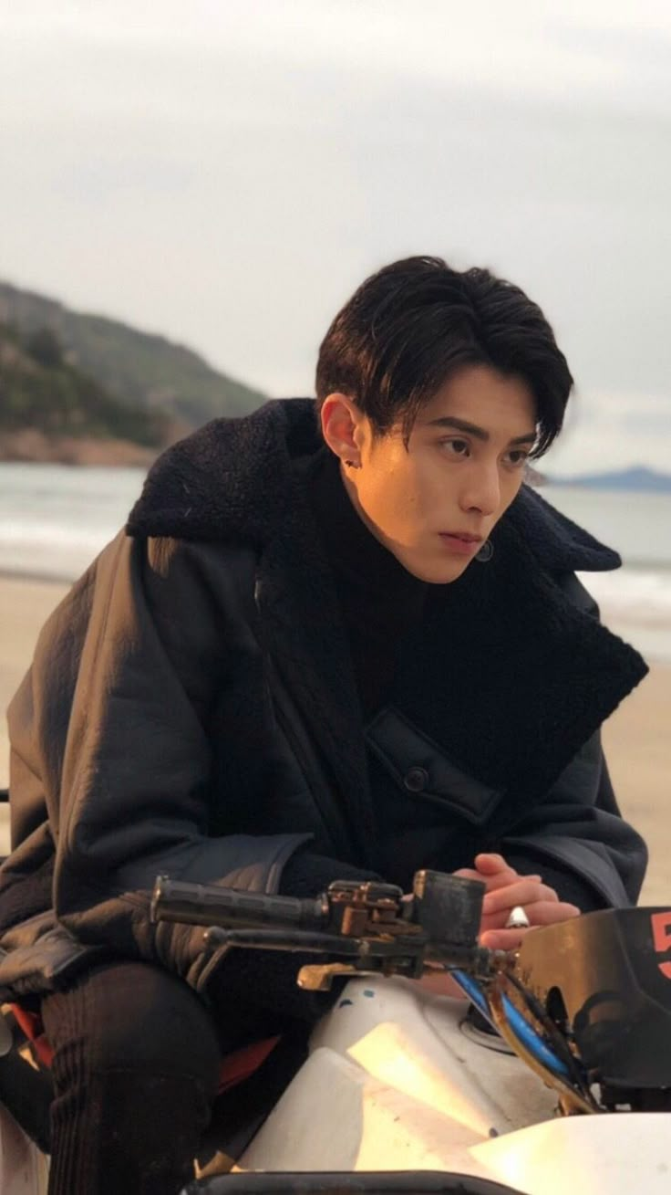 a young man sitting on top of a motorcycle next to the ocean