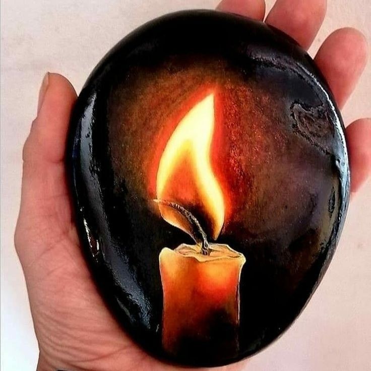 a hand holding a lit candle painted on a black rock with orange flames in the center