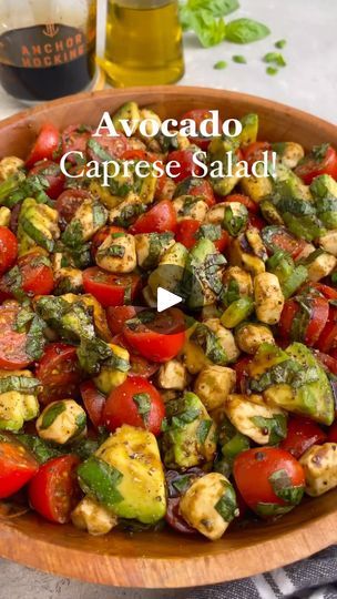 a wooden bowl filled with lots of different types of vegetables next to a bottle of olive oil