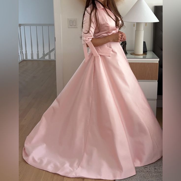 a woman in a long pink dress and hat poses for a photo with her hands on her hips