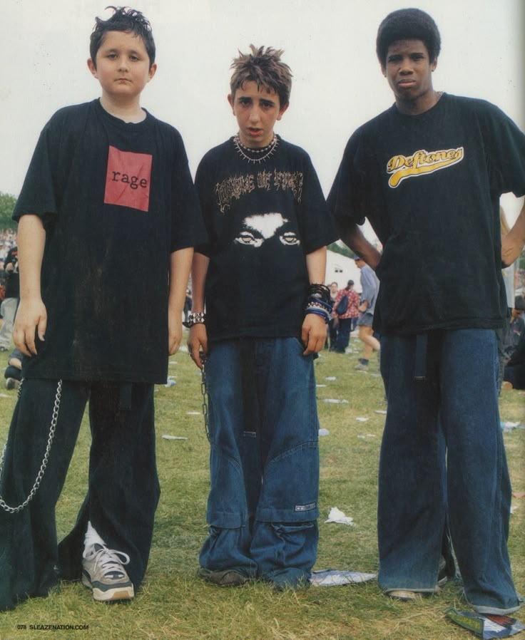 three young men standing next to each other on top of a grass covered field with people in the background