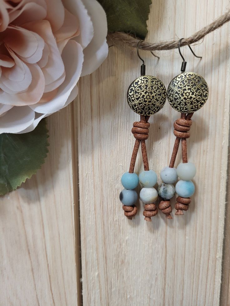 Ornate bronze button earrings with marbled teal colored stone beads on brown leather cord. Brown Adjustable Earrings With Natural Stones, Adjustable Earthy Dangle Earrings, Adjustable Brown Drop Earrings, Brown Adjustable Drop Earrings, Adjustable Bohemian Patina Earrings, Handmade Adjustable Bronze Earrings, Rustic Adjustable Copper Earrings, Brown Earrings With Natural Stones And Round Beads, Casual Adjustable Nickel-free Earrings