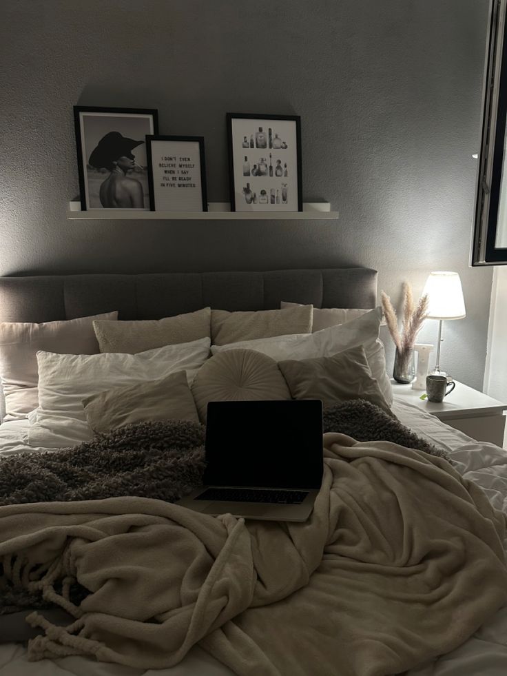 a laptop computer sitting on top of a bed covered in blankets and throw pillows with pictures above it