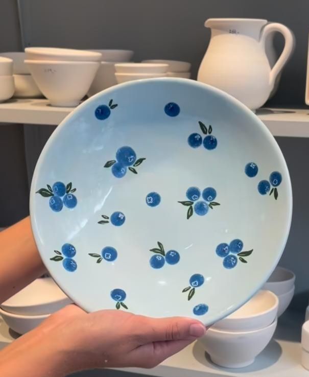 a person holding a bowl with blueberries on it in front of plates and bowls