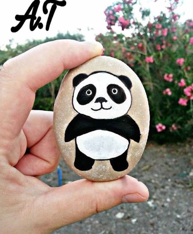 a hand holding a rock with a panda bear painted on it