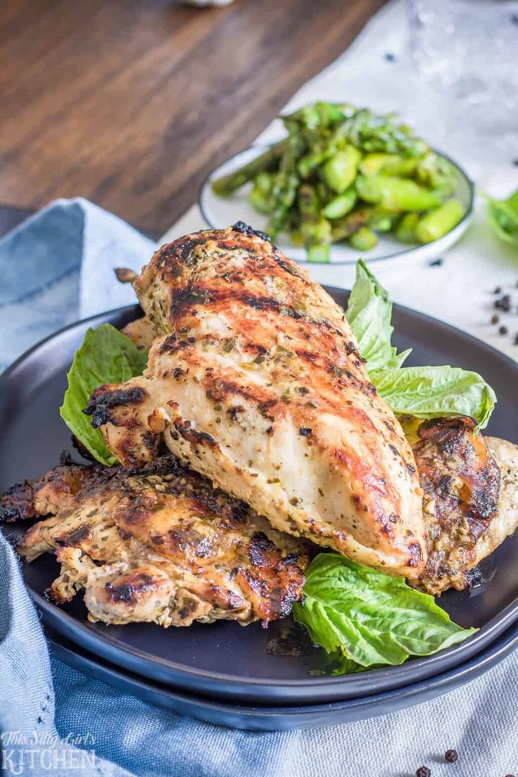 grilled chicken on a black plate with lettuce and other vegetables next to it