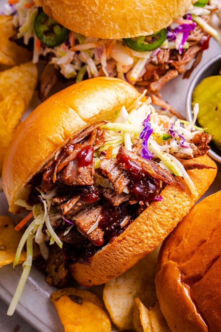 two pulled pork sandwiches with coleslaw, slaw and pickles on the side