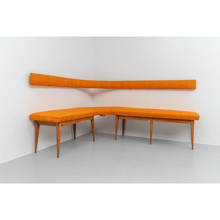 an orange bench sitting next to a white wall with two wooden benches on top of it