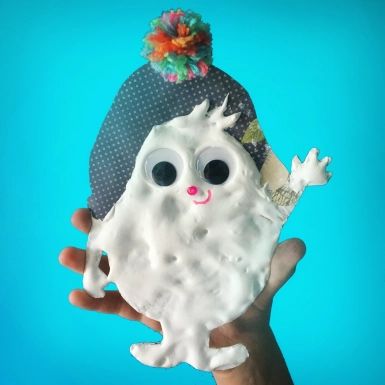 a hand holding a fake white ghost with big eyes and a hat on it's head