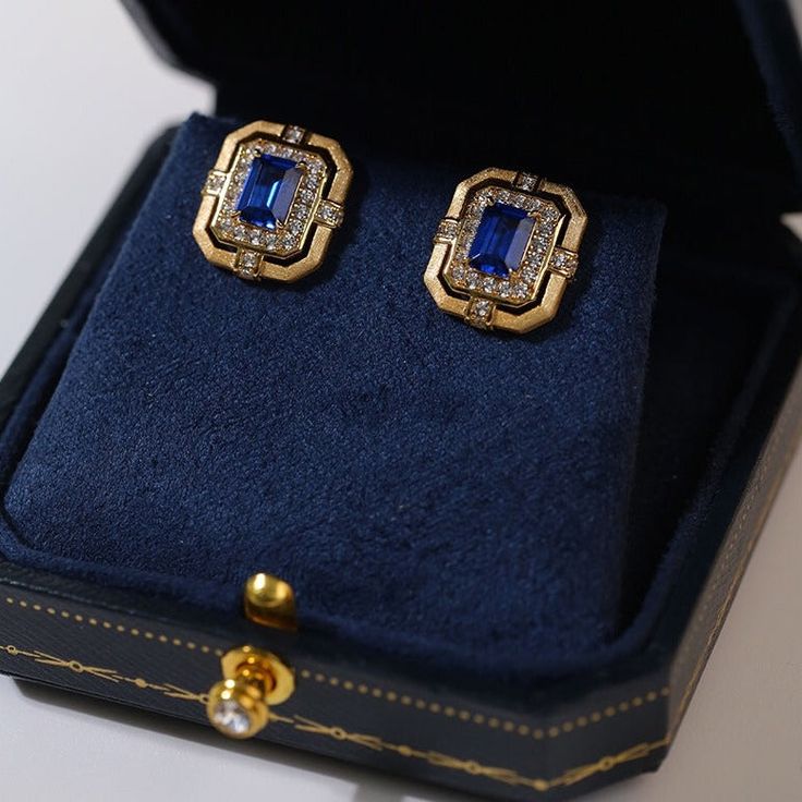 Featuring a delicate square design, these matte gold square hollow diamond wrapped sapphire stud earrings are crafted in matte gold with intricate diamond detailing and a stunning sapphire in the center. Unique cutout patterns add a modern touch to a classic silhouette. Metal: 18K Recycled Gold Plated Vermeil on Recycled Sterling Silver Gemston: Diamond,Cubic Zirconia Earring Diameter: 15mm Single Weight: 3.5g Gold Cubic Zirconia Earrings With Gemstones, Sapphire Earrings With Diamond Accents For Evening, Evening Earrings With Sapphire And Diamond Accents, Evening Sapphire Earrings With Diamond Accents, Luxury Rectangular Diamond Earrings, Elegant Square Cut Diamond Earrings, Elegant Rectangular Jewelry For Evening, Elegant Square Cut Earrings For Anniversary, Luxury Rectangular Earrings For Evening