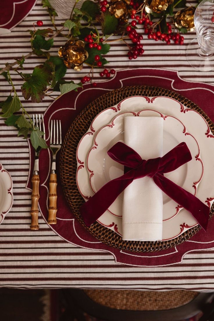 the place setting is set with red and white plates, silverware, and holly leaves