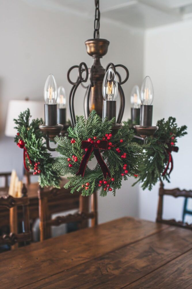 a chandelier hanging from the ceiling with candles and holly wreaths on it