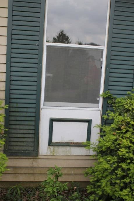 an open window on the side of a house with green shutters and bushes around it