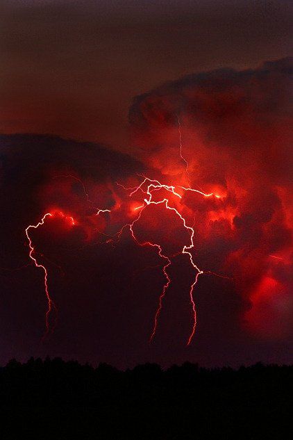 the sky is dark and red as lightning strikes in the distance, with some clouds behind it