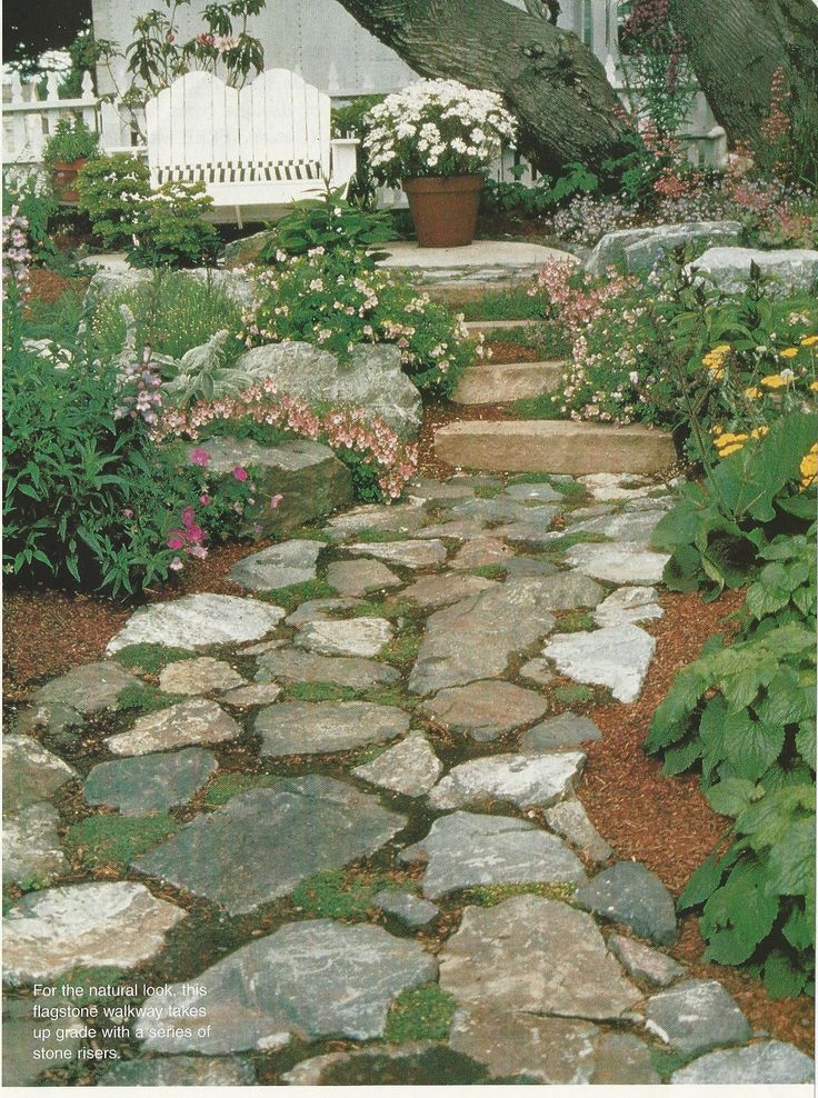 a stone path in front of a white house with flowers and trees on either side