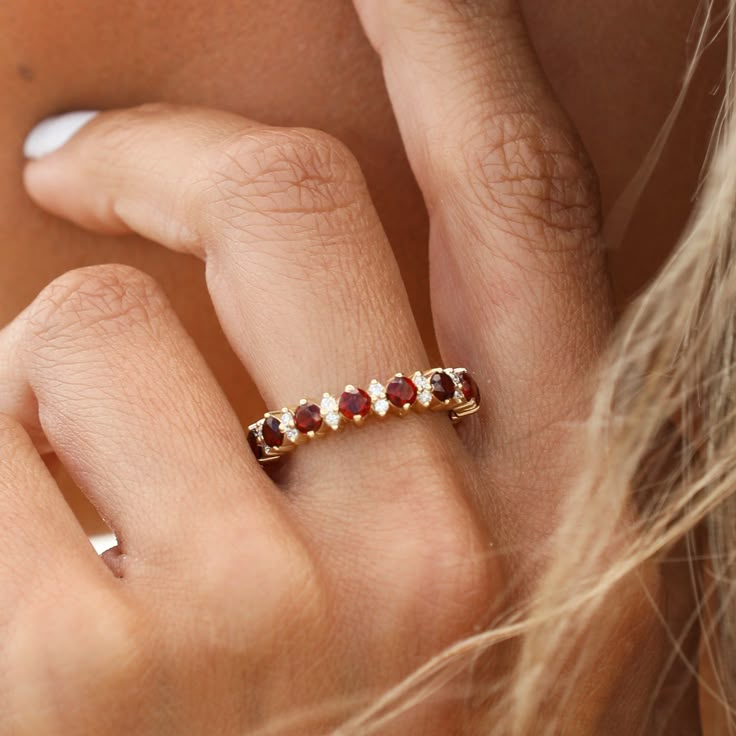 a woman's hand wearing a gold ring with three red and white stones on it