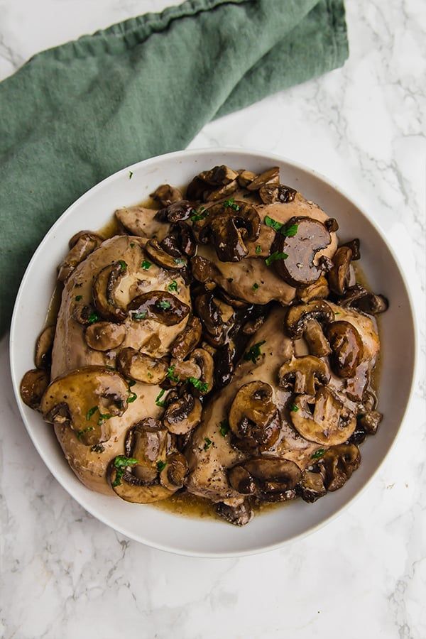 a white bowl filled with mushrooms and sauce on top of a marble counter next to a green napkin