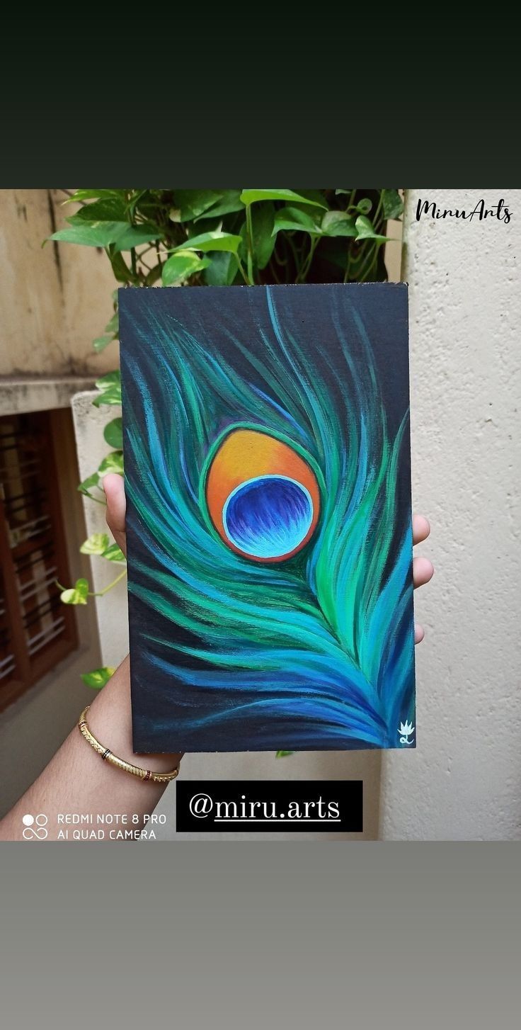 a person holding up a piece of art with a peacock feather painted on it's side