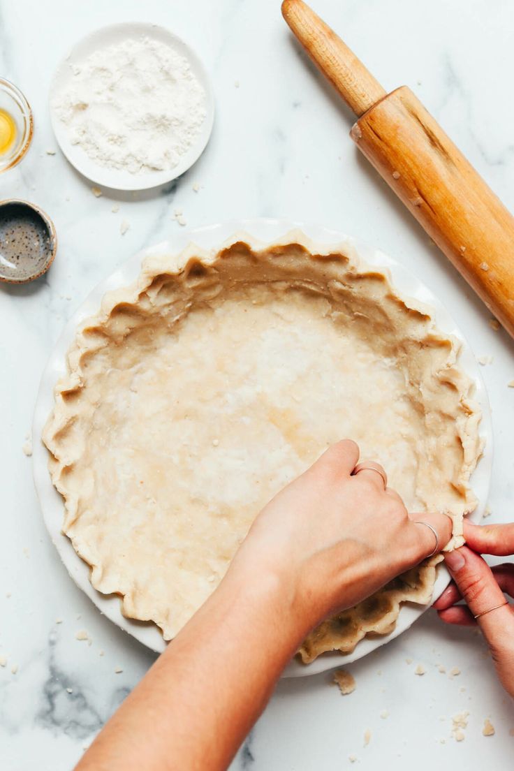 a person is making an uncooked pie crust on a marble table with ingredients nearby