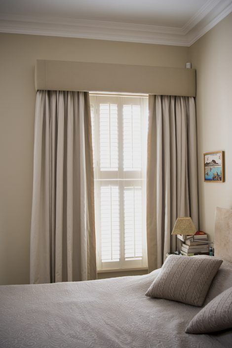 a bed sitting next to a window in a room with white curtains and a lamp