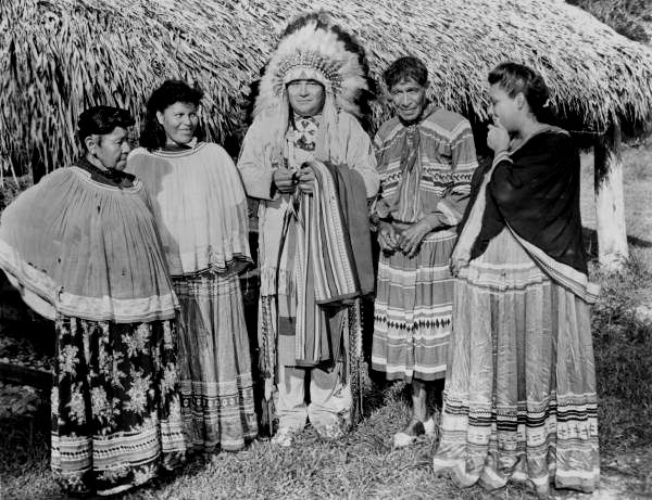 an old black and white photo of native american women standing in front of a hut