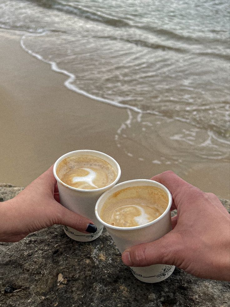 two people holding cups of coffee near the ocean