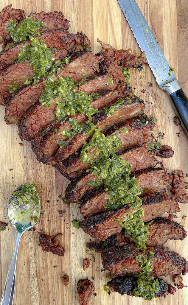 sliced steak with green sauce on wooden cutting board