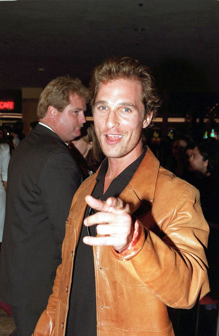 a man in a brown leather jacket pointing at the camera with his right hand out