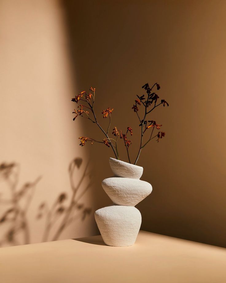 three white vases with flowers in them on a table next to a brown wall