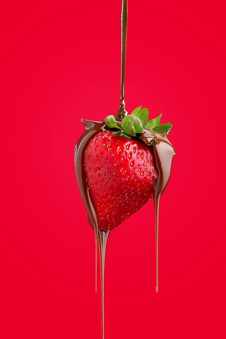 a chocolate covered strawberry hanging from a hook on a red background with melted chocolate and green leaves