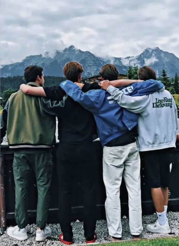 four people are standing in front of a truck with their arms around each other and looking at the mountains