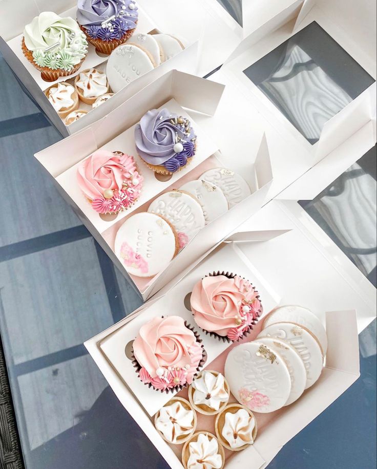 three boxes filled with different types of cupcakes on top of a glass table