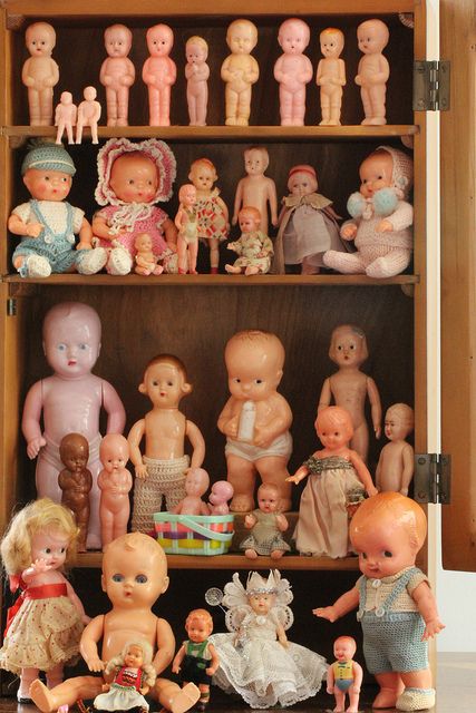 a cabinet filled with lots of different types of dolls on top of wooden shelves next to each other