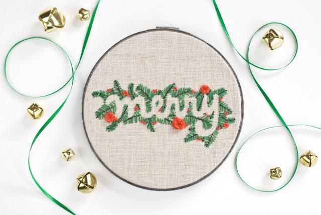 a cross stitch christmas ornament with the word merry surrounded by holly and red berries