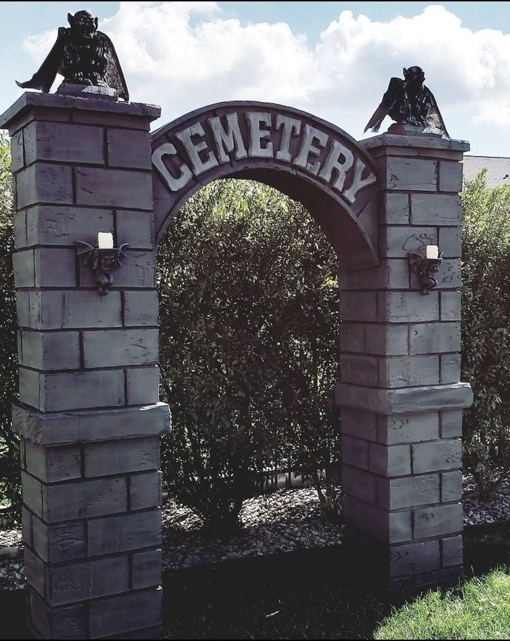 two statues sitting on top of a stone arch in the middle of a park area