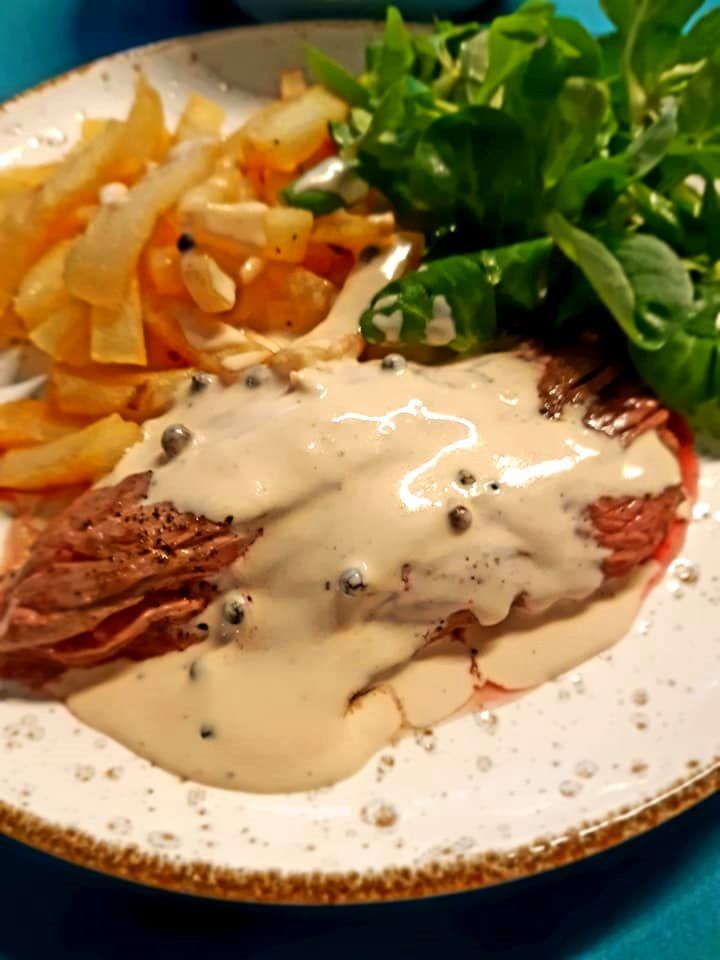 a white plate topped with meat covered in gravy next to french fries and lettuce