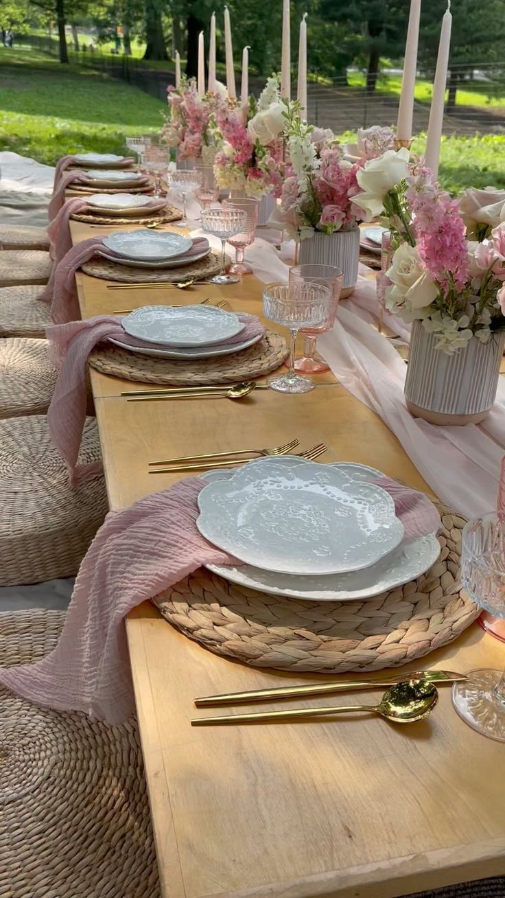 the table is set with pink and white flowers in vases, candles, and plates