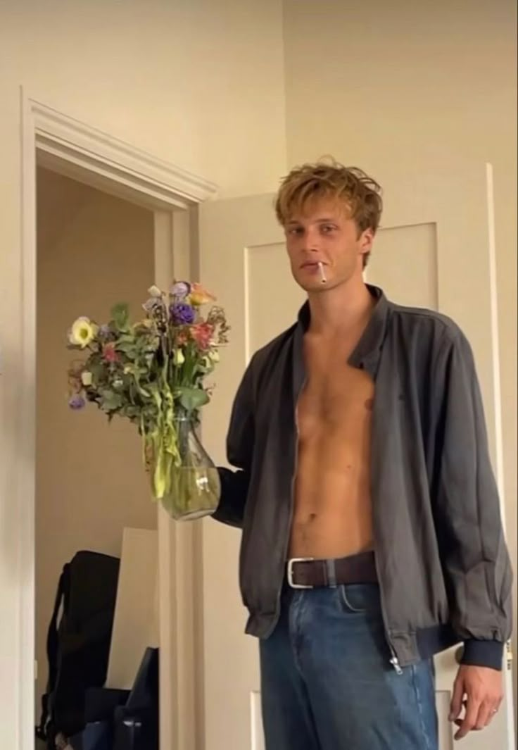 a shirtless man standing in front of a mirror holding a vase with flowers on it