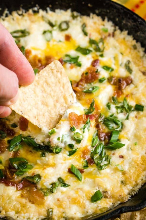 a hand dipping a tortilla chip into a skillet filled with cheese and spinach