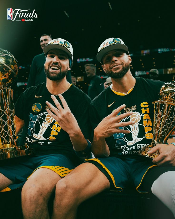 two men sitting next to each other with trophies in front of their faces and hands