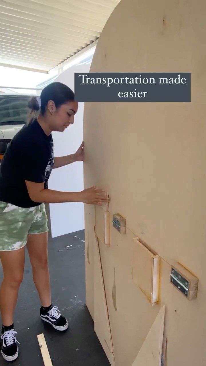 a woman in black shirt and green shorts standing next to a wall with holes on it