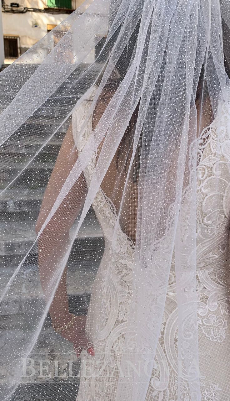 a woman wearing a wedding veil on top of her head walking down the stairs in front of a building