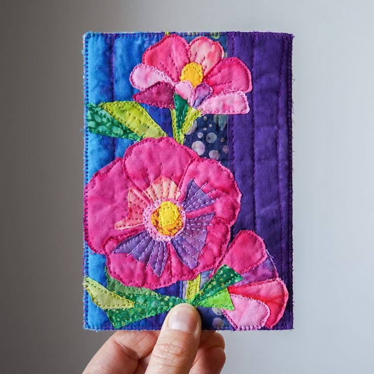 a hand holding up a piece of fabric with pink flowers on purple and blue squares